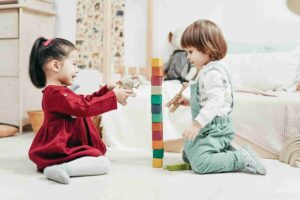 Boy In White Long Sleeve Shirt And Green Pants Sitting On Floor Beside Girl In Red 3661452 Scaled 1